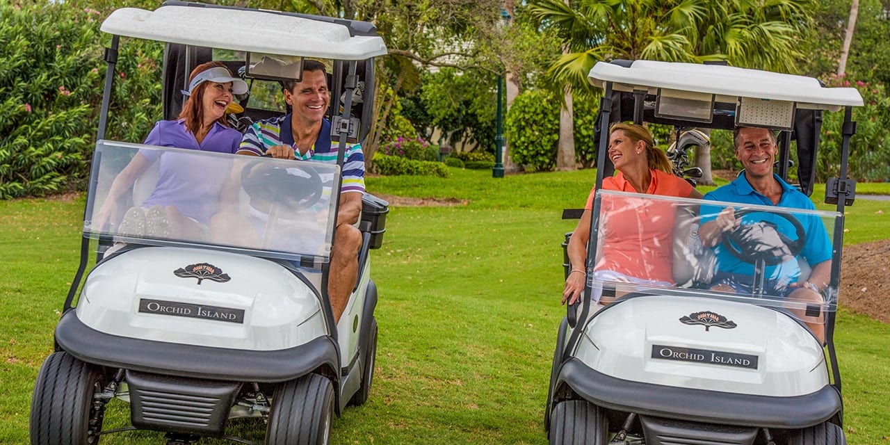 Two couples drive Orchid Island Golf Carts along the golf course.