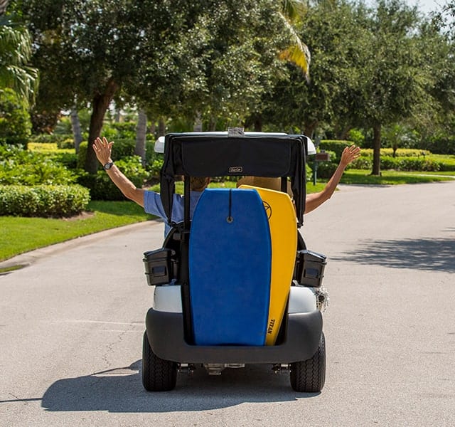 Two Orchid Island Members Riding a Golf Cart carrying two boogie boards.
