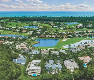Aerial view of homes, waterways, golf course, and ocean beyond.