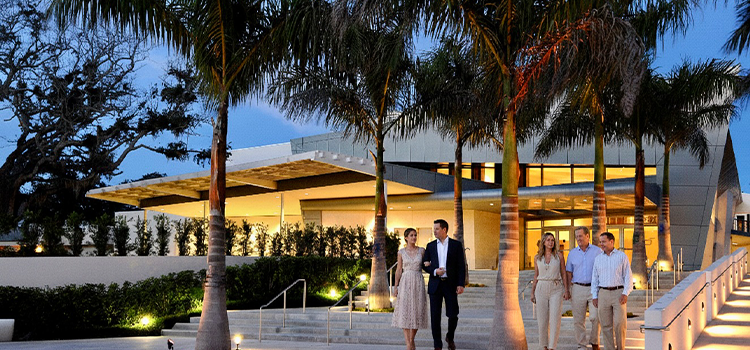Guests walking toward a modern theater under palm trees at dusk.