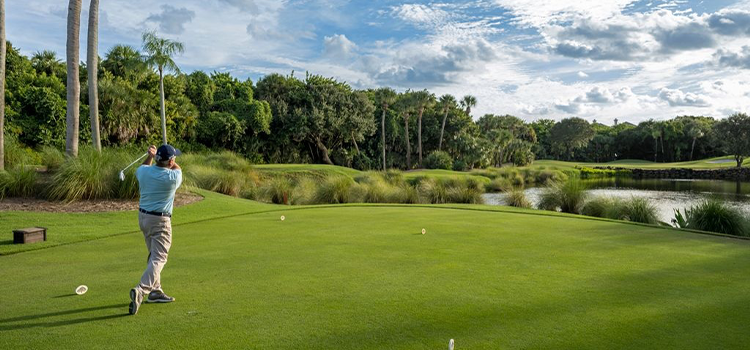Golfer swinging club on green course beside water