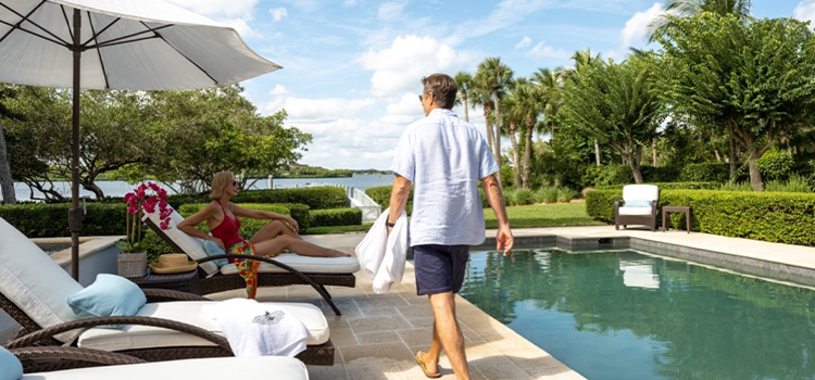 Two adults relaxing on lounge chairs beside an outdoor swimming pool.