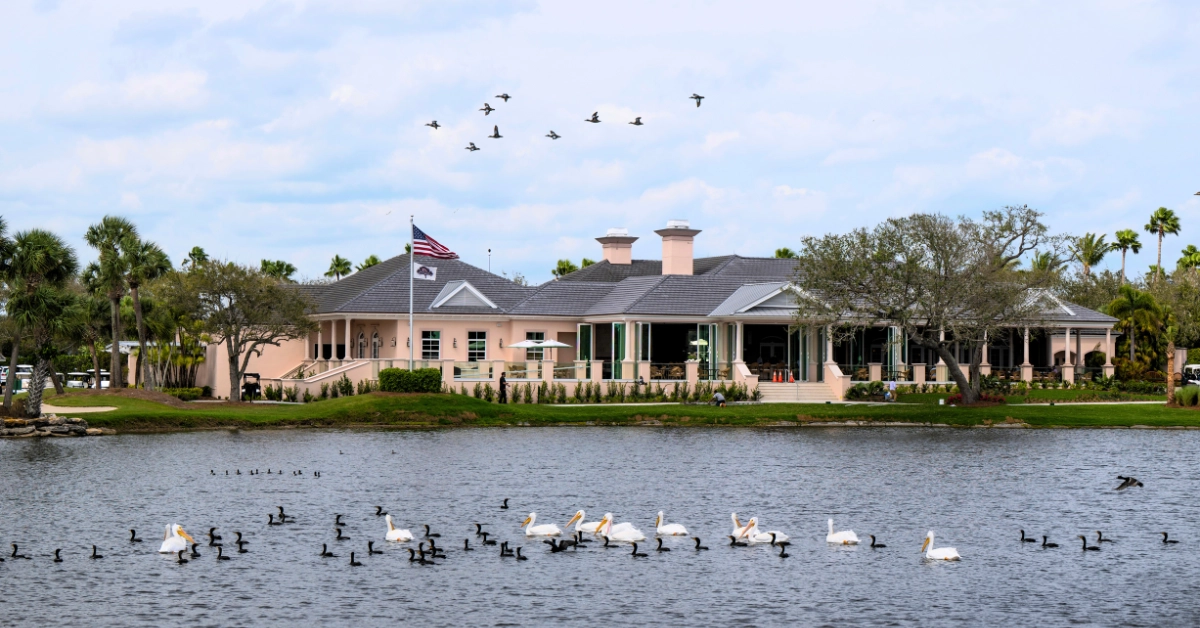 Clubhouse building beside lagoon waters with birds and coastal landscape