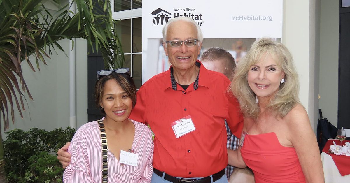 Three adults smiling at Habitat for Humanity event with banner behind them